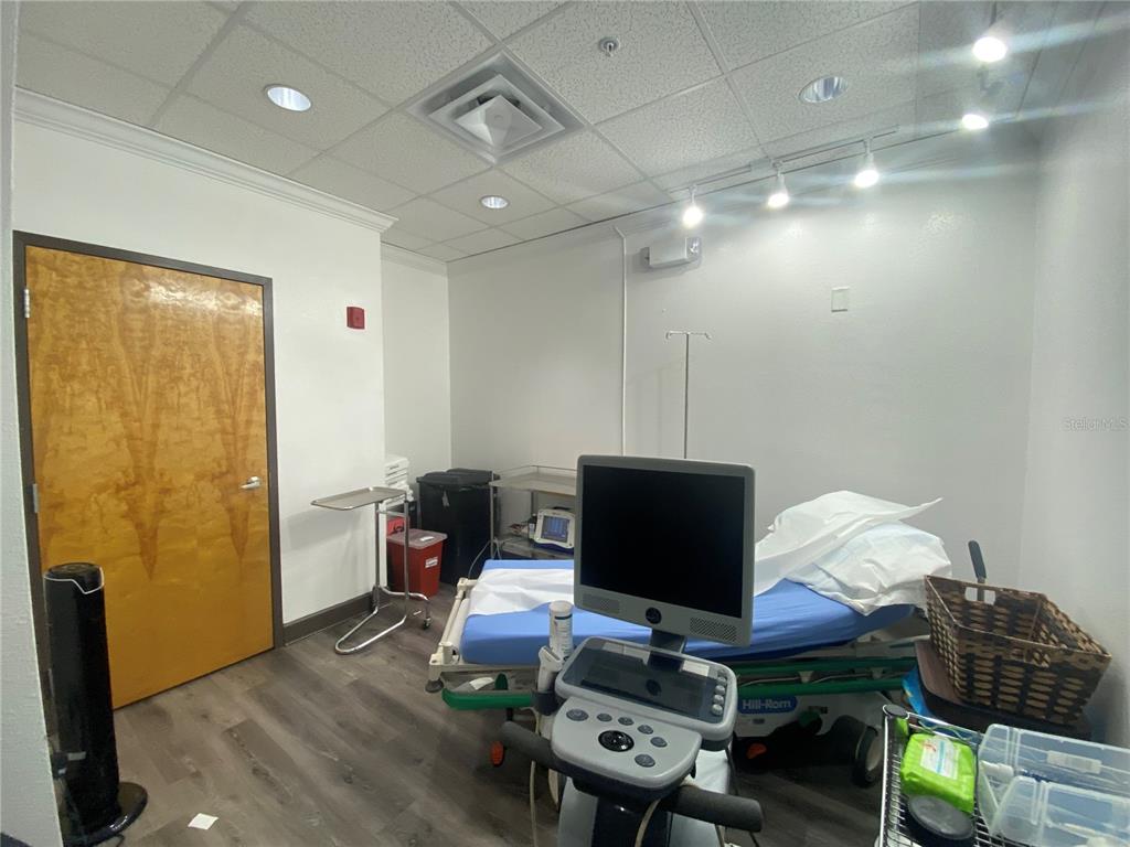 A medical examination room features a hospital bed, a monitor, and wood-look flooring — 566 OCOEE COMMERCE PARKWAY, OCOEE, FL