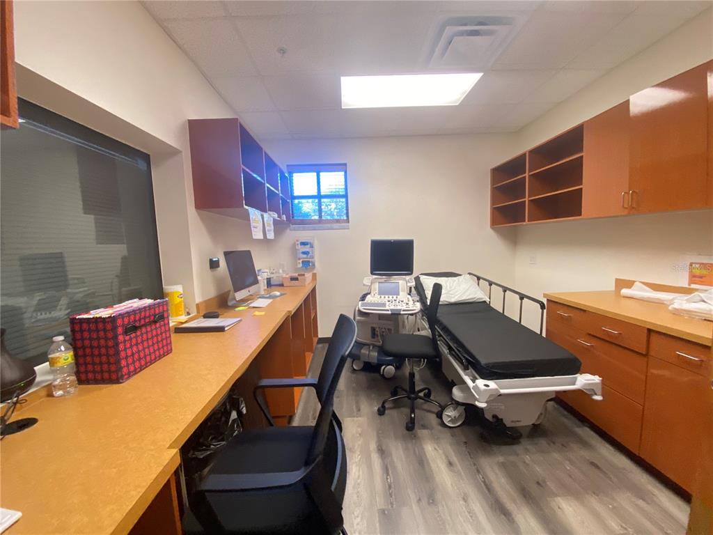 A medical examination room features a patient bed, ultrasound equipment, wooden cabinetry, and a desk — 566 OCOEE COMMERCE PARKWAY, OCOEE, FL