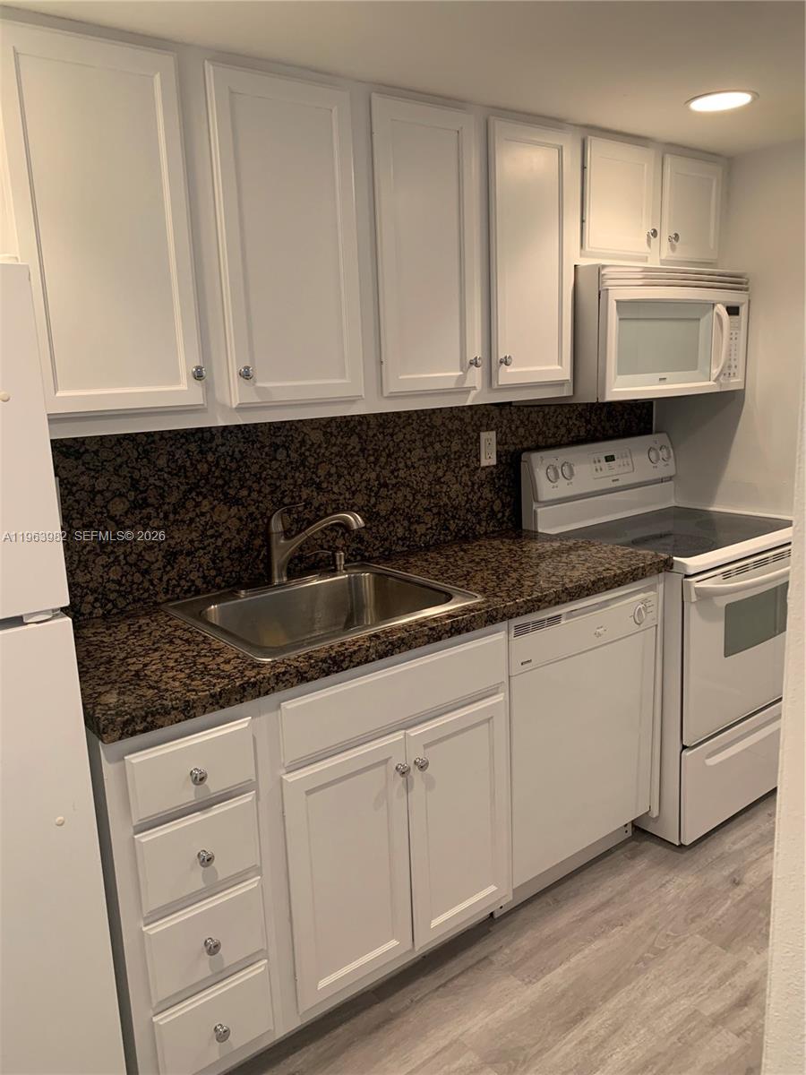 A kitchen features white cabinets, dark granite countertops, and white appliances — 290 Sunrise Dr # 304, Key Biscayne FL 33149, KEY BISCAYNE, FL