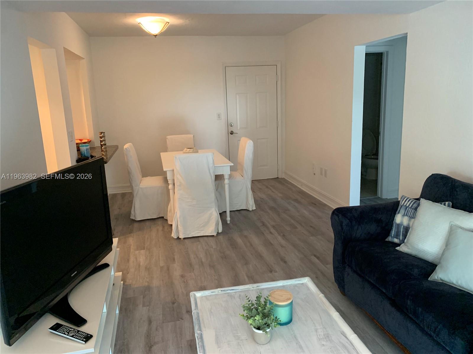 A living and dining area features light wood-look flooring, white furniture, and a dark sofa — 290 Sunrise Dr # 304, Key Biscayne FL 33149, KEY BISCAYNE, FL