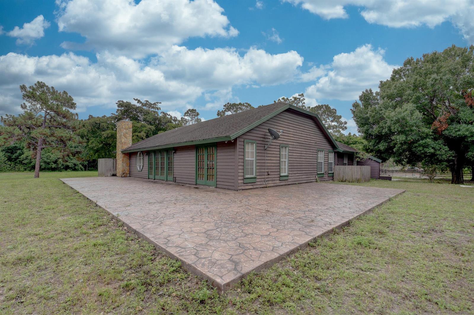 A brown wood-sided house features a large stamped concrete patio and a stone chimney — 19153 Eagles Way Court, Loxahatchee FL 33470, LOXAHATCHEE, FL
