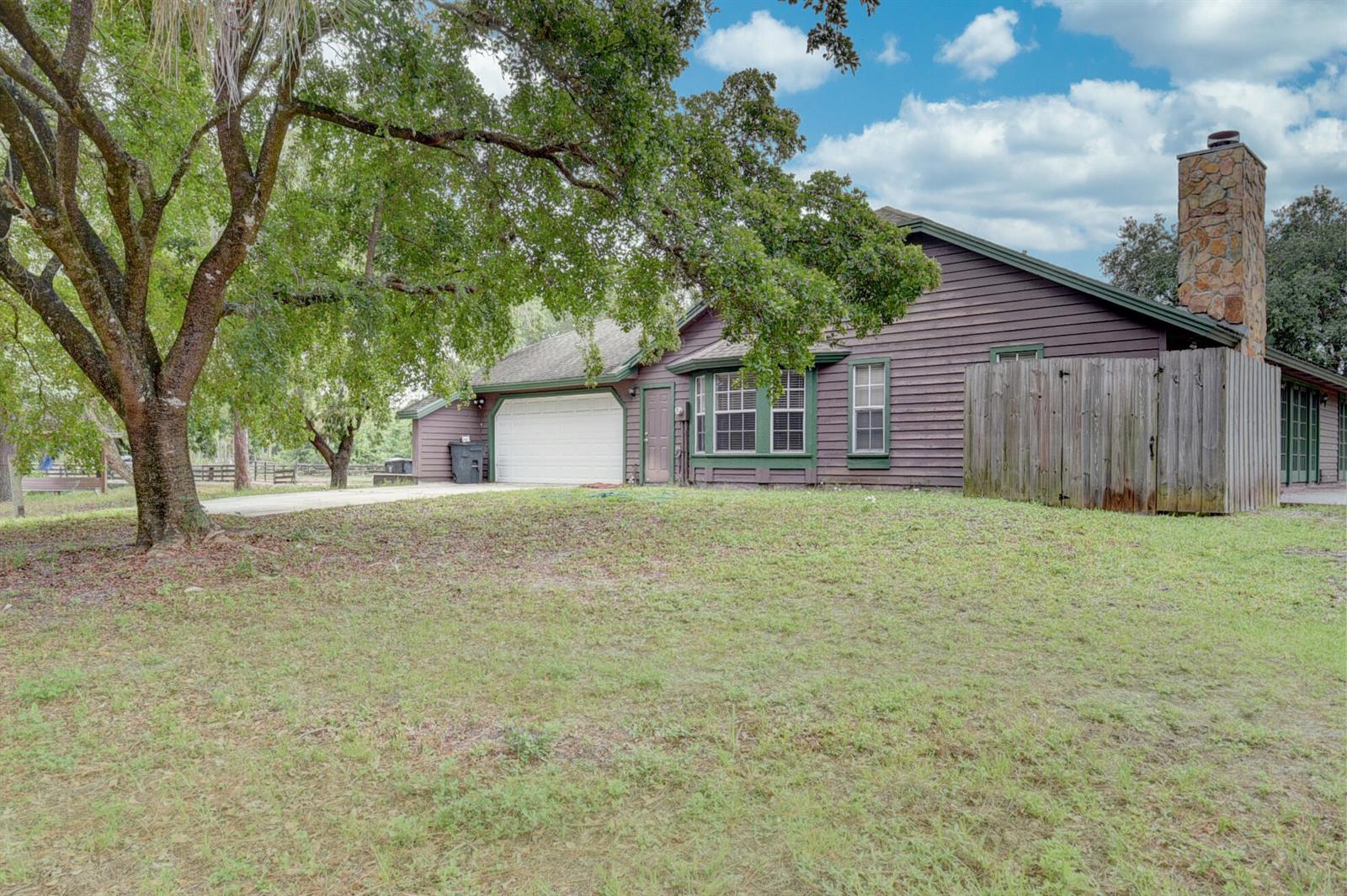 A brown wood-sided house with a stone chimney, a garage, and a large front lawn — 19153 Eagles Way Court, Loxahatchee FL 33470, LOXAHATCHEE, FL