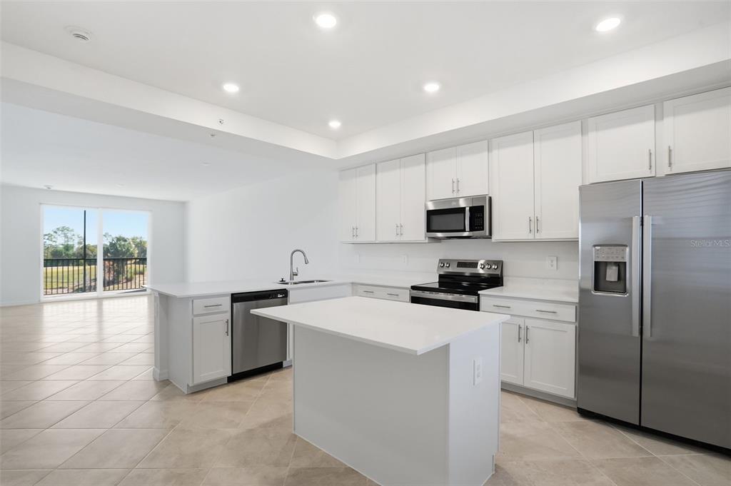 A modern kitchen features white cabinetry, stainless steel appliances, a center island, and tile flooring — 19110 SCALLOP LOOP UNIT 204, LAKEWOOD RANCH, FL