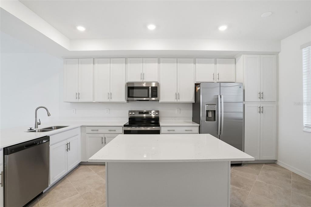 A modern kitchen features white cabinets, stainless steel appliances, a center island, and tile flooring — 19110 SCALLOP LOOP UNIT 204, LAKEWOOD RANCH, FL