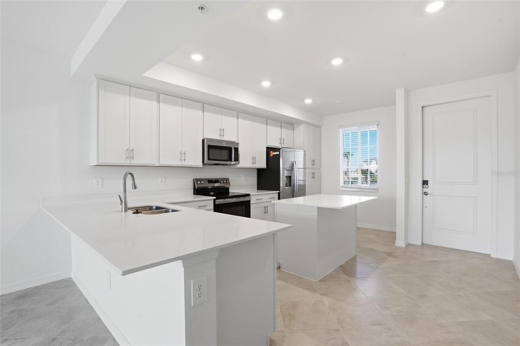 A modern kitchen features white cabinets, quartz countertops, a center island, and stainless steel appliances — 19110 SCALLOP LOOP UNIT 204, LAKEWOOD RANCH, FL