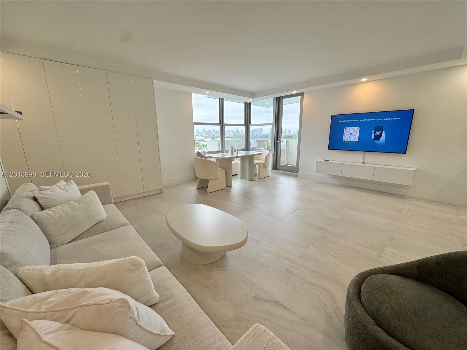 A modern living room features light tile floors, a white sofa, and a wall-mounted television — 2899 Collins Ave # 1414, Miami Beach FL 33140, MIAMI BEACH, FL