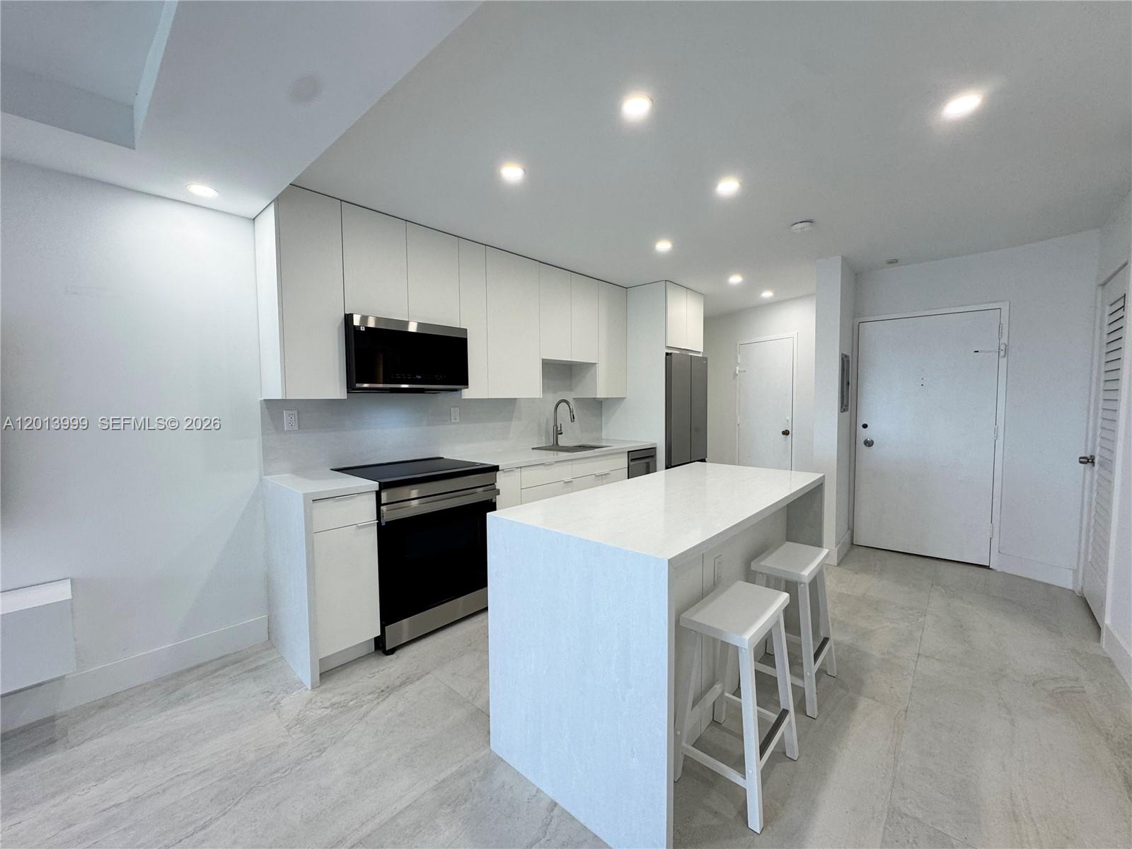 A modern kitchen features white cabinetry, stainless steel appliances, and a central island with stools — 2899 Collins Ave # 1414, Miami Beach FL 33140, MIAMI BEACH, FL