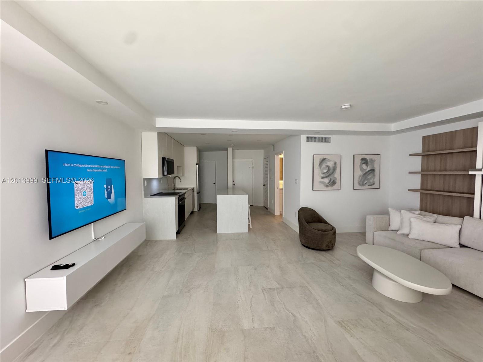 A modern living room features light tile floors, a wall-mounted television, and an open kitchen — 2899 Collins Ave # 1414, Miami Beach FL 33140, MIAMI BEACH, FL