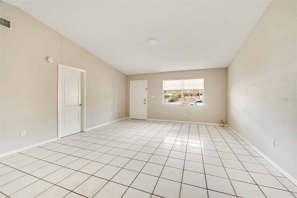 An empty room with white tile flooring, beige walls, a white door, and a window — 4715 GREENHILL STREET, COCOA, FL