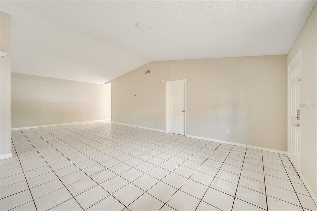 An empty room with white tile flooring, beige walls, and a vaulted ceiling — 4715 GREENHILL STREET, COCOA, FL