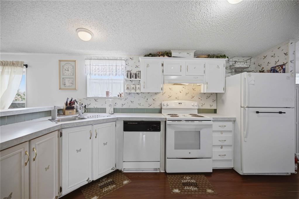 A kitchen features white cabinets, white appliances, patterned wallpaper, and dark wood-look flooring — 6720 NE 1ST PLACE, OCALA, FL