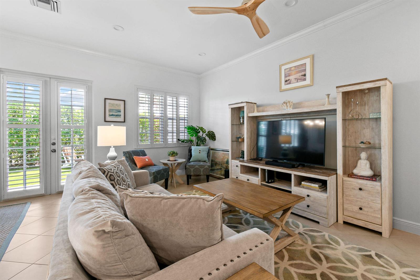 A living room features a beige sofa, wooden coffee table, media console, and a ceiling fan — 106 Ocean Breeze Drive, Juno Beach FL 33408, JUNO BEACH, FL