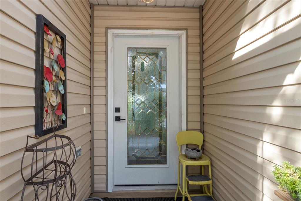 A white front door with a decorative glass insert sits between beige vinyl siding walls — 521 SAN PEDRO DRIVE, THE VILLAGES, FL
