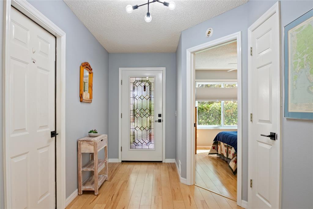 An entryway with light wood floors, a decorative glass front door, and a bedroom view — 521 SAN PEDRO DRIVE, THE VILLAGES, FL