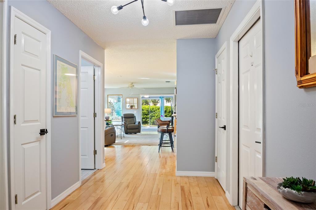 A hallway with light wood floors leads toward an open living area with a patio view — 521 SAN PEDRO DRIVE, THE VILLAGES, FL
