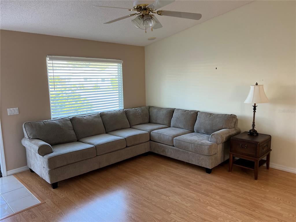 A living room features a large gray sectional sofa, a side table with a lamp, and wood-look flooring — 1232 ZAPATA PLACE, LADY LAKE, FL