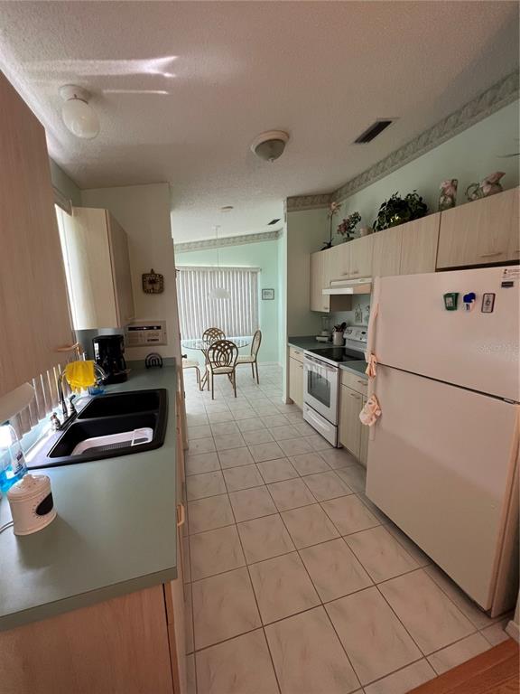 A kitchen with light wood cabinets, white appliances, and a teal countertop leads to a dining area — 1232 ZAPATA PLACE, LADY LAKE, FL