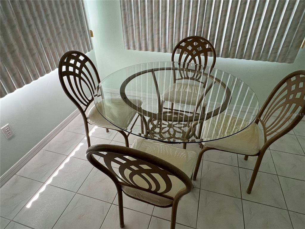 A round glass-topped dining table with four metal chairs sits on a tiled floor — 1232 ZAPATA PLACE, LADY LAKE, FL
