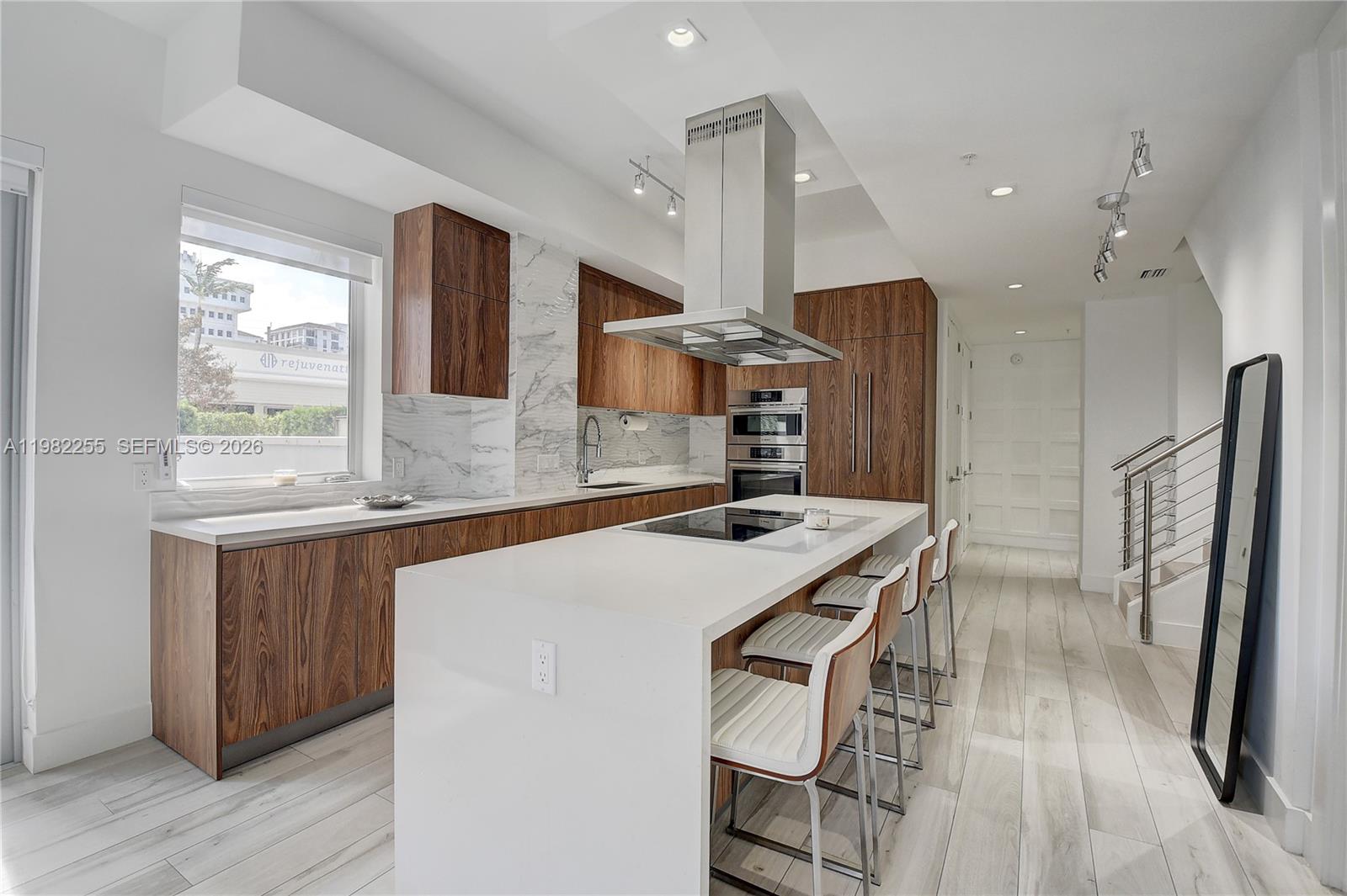 A modern kitchen features wood-grain cabinetry, white countertops, a central island, and stainless steel appliances — 155 E Boca Raton Rd, Boca Raton FL 33432, BOCA RATON, FL