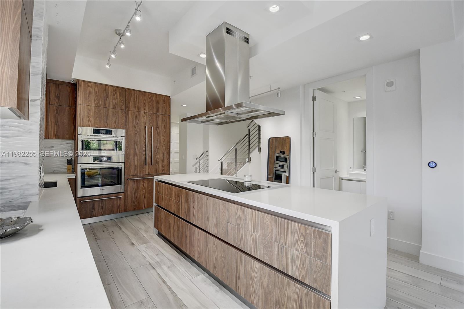 A modern kitchen features wood-grain cabinetry, a large white island with a cooktop, and stainless-steel appliances — 155 E Boca Raton Rd, Boca Raton FL 33432, BOCA RATON, FL