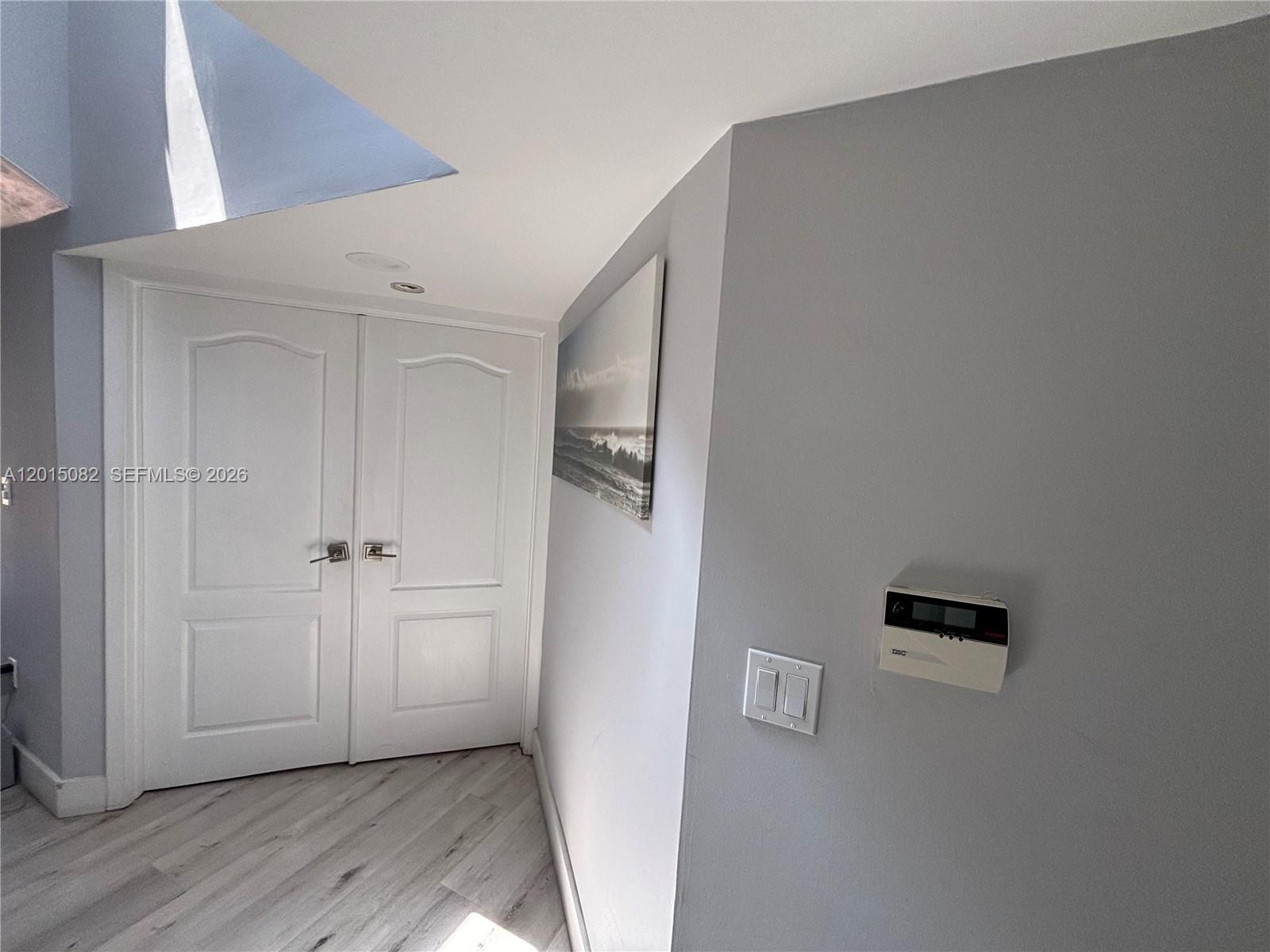 A hallway features light wood-look flooring, white double doors, a wall-mounted thermostat, and artwork — 12922 SW 88th Ter # 206, Miami FL 33186, MIAMI, FL