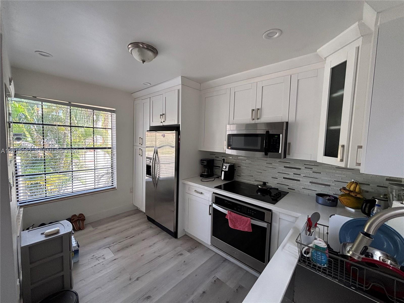 A kitchen features white cabinets, stainless steel appliances, a tiled backsplash, and light wood flooring — 12922 SW 88th Ter # 206, Miami FL 33186, MIAMI, FL