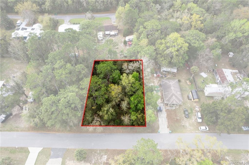 An aerial view shows a rectangular, wooded vacant lot outlined in red along a road — 7654 W SUNBURST LANE, HOMOSASSA, FL