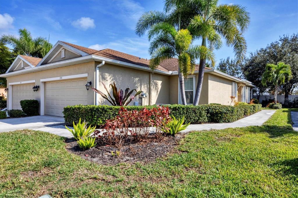 A tan single-story house with a two-car garage, palm trees, and a landscaped front yard — 2520 TERRACINA DRIVE, VENICE, FL