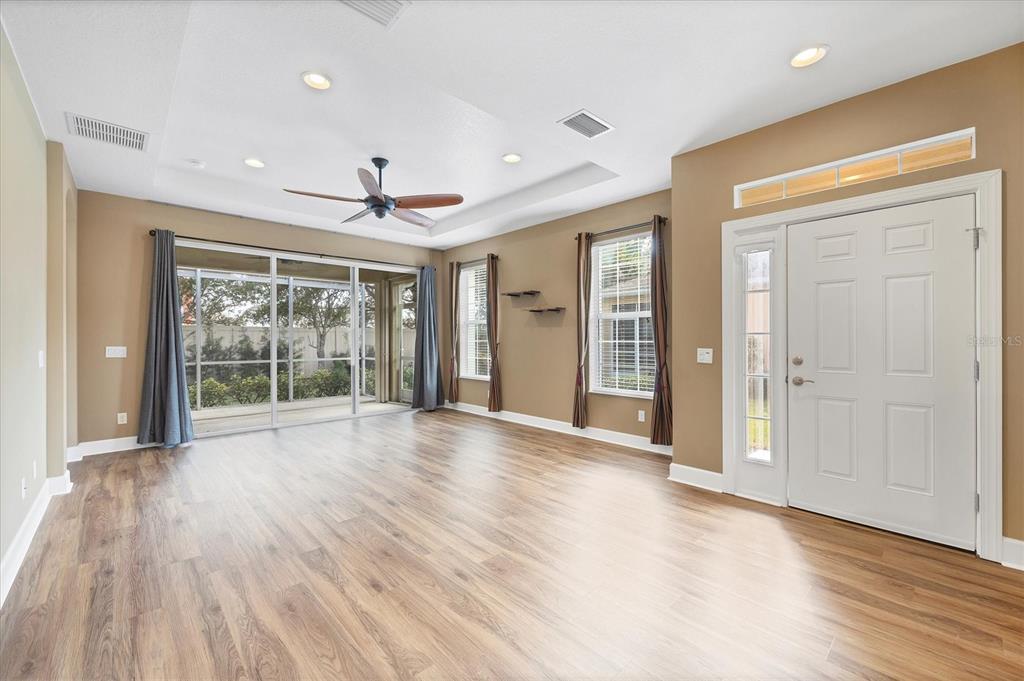 A living room with wood-look flooring, a tray ceiling, sliding glass doors, and a front door — 2520 TERRACINA DRIVE, VENICE, FL