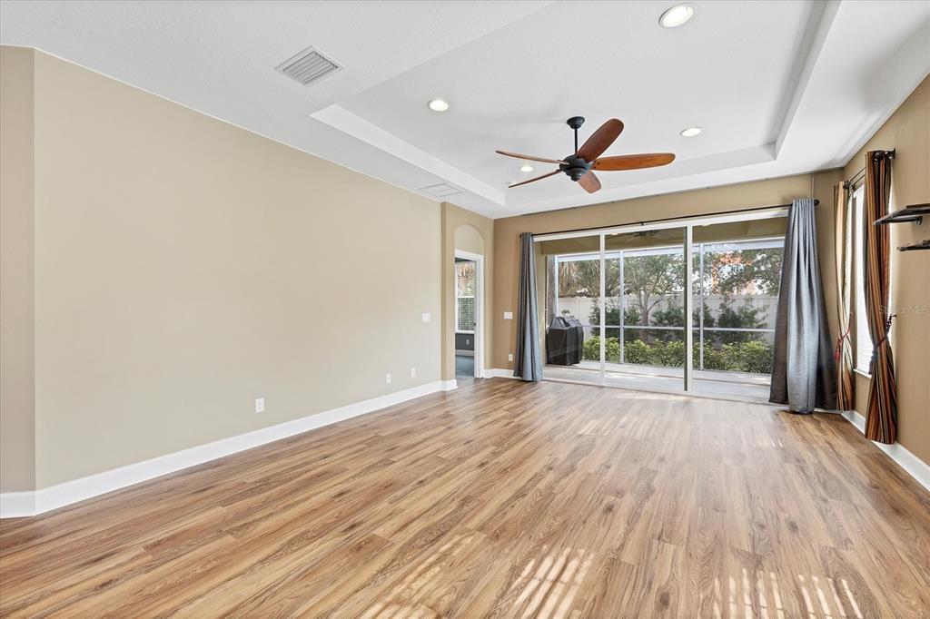 An empty living room features wood-look flooring, a tray ceiling with a fan, and sliding doors — 2520 TERRACINA DRIVE, VENICE, FL