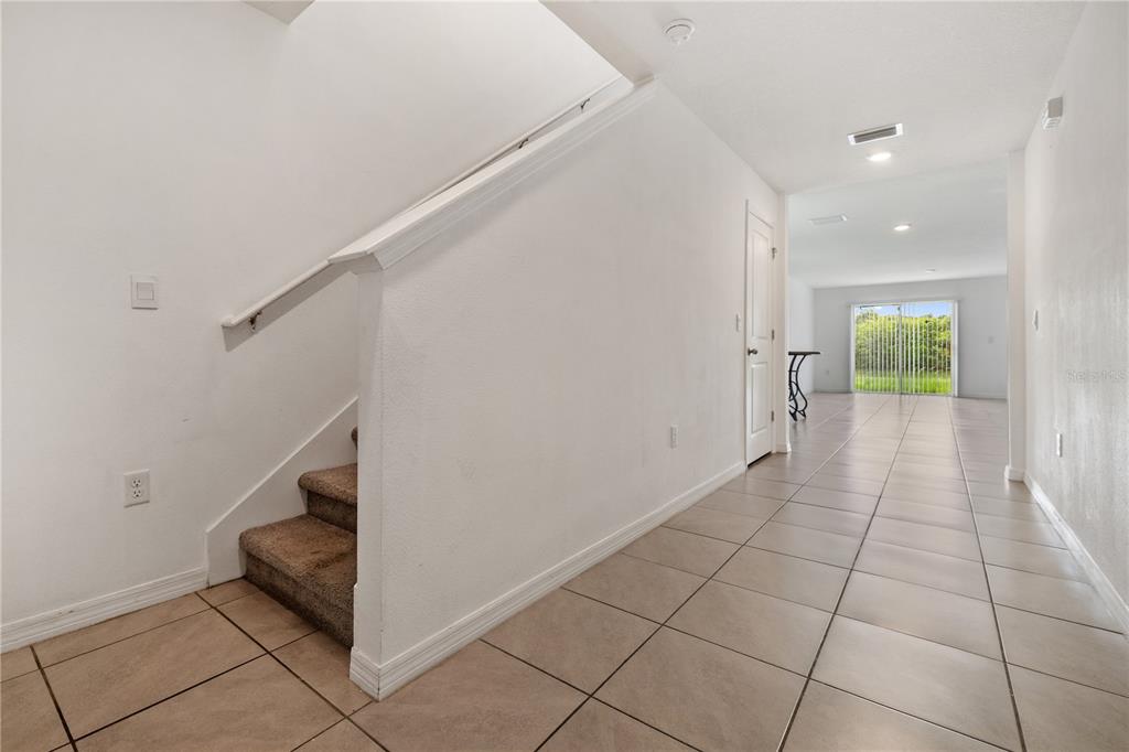A hallway with tiled floors leads toward a sliding glass door past a carpeted staircase — 11926 DOWNY BIRCH DRIVE, RIVERVIEW, FL