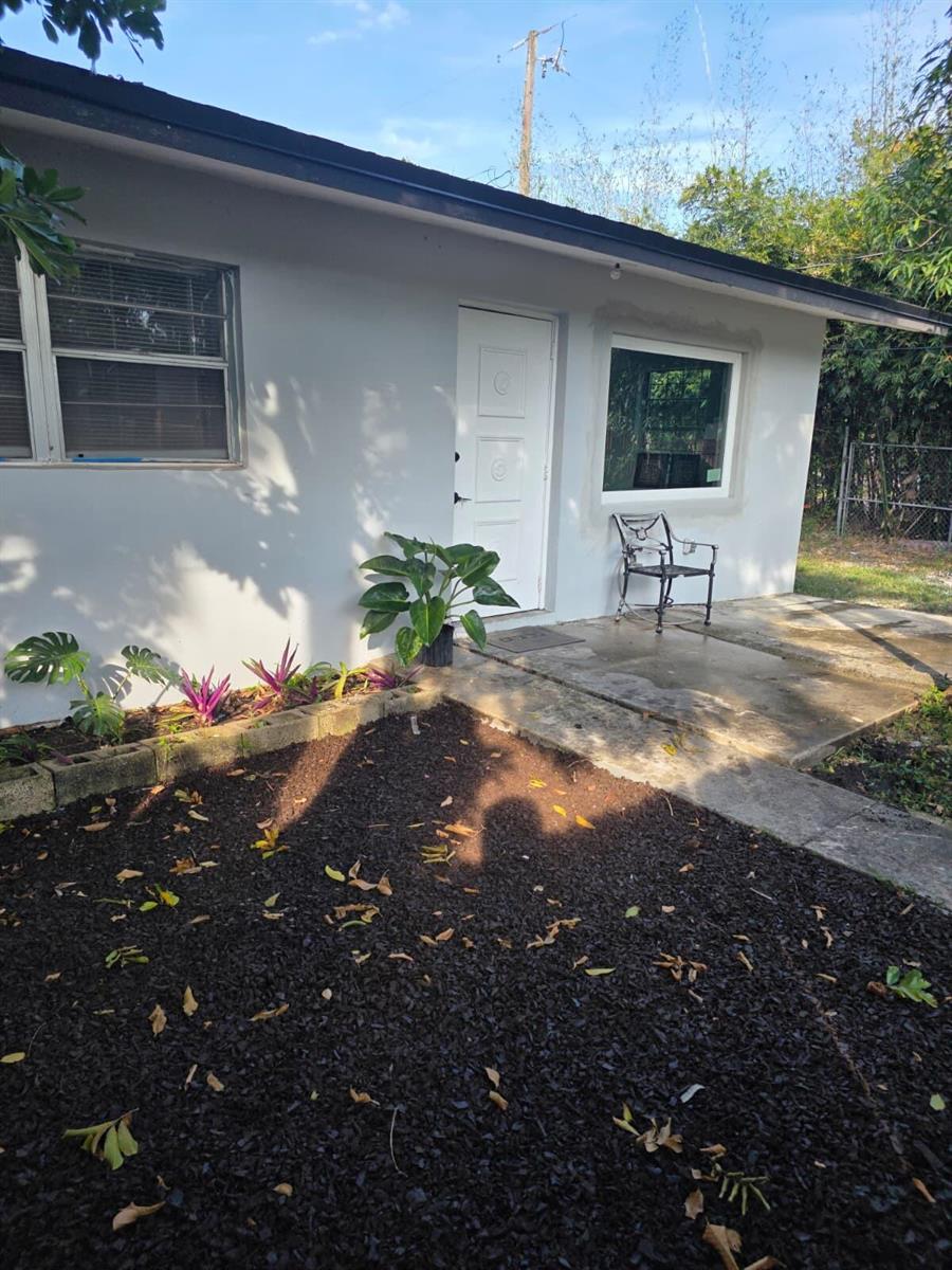 A light gray house exterior features a white front door, a window, and landscaped garden beds — 3386 Rudolph Road, FL 33461, FL