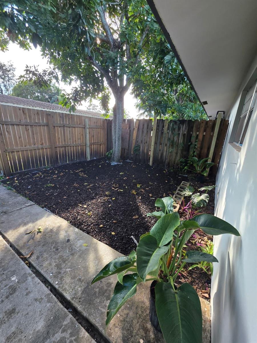 A fenced backyard features a large tree, dark mulch ground cover, and a concrete patio — 3386 Rudolph Road, FL 33461, FL