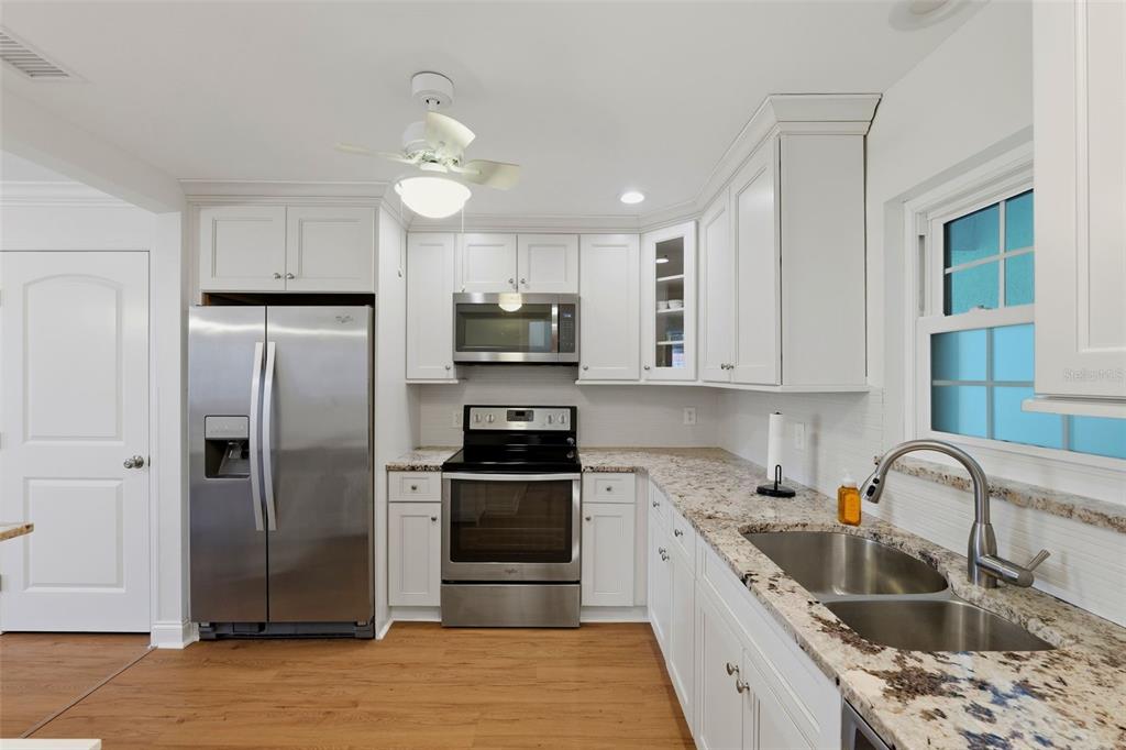 A kitchen features white cabinetry, stainless steel appliances, granite countertops, and light wood flooring — 1706 BELLEAIR FOREST DRIVE UNIT 234, BELLEAIR, FL