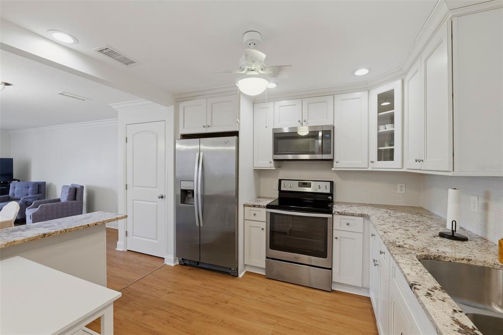 A kitchen features white cabinets, granite countertops, stainless steel appliances, and light wood flooring — 1706 BELLEAIR FOREST DRIVE UNIT 234, BELLEAIR, FL