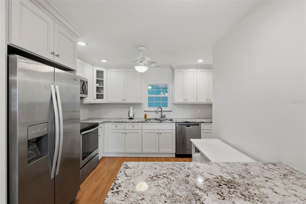 A kitchen features white cabinets, granite countertops, stainless steel appliances, and light wood flooring — 1706 BELLEAIR FOREST DRIVE UNIT 234, BELLEAIR, FL
