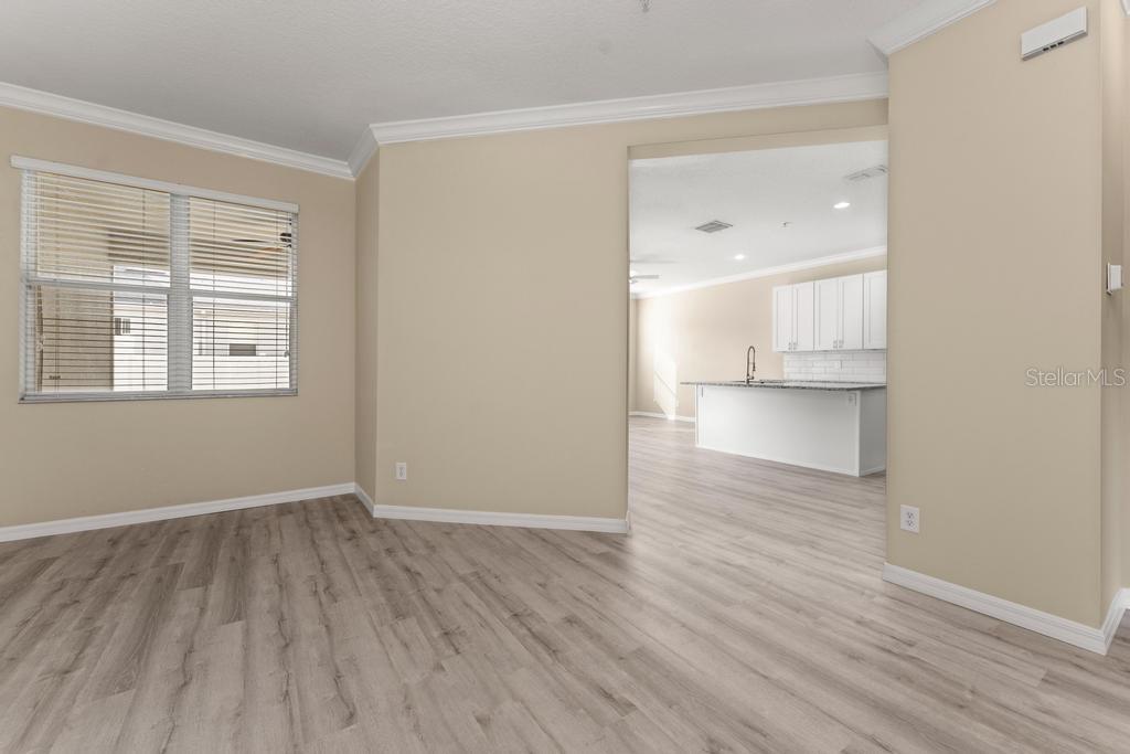A living area with light wood-look flooring opens into a kitchen with white cabinets — 868 STONECHASE LANE, LAKE MARY, FL