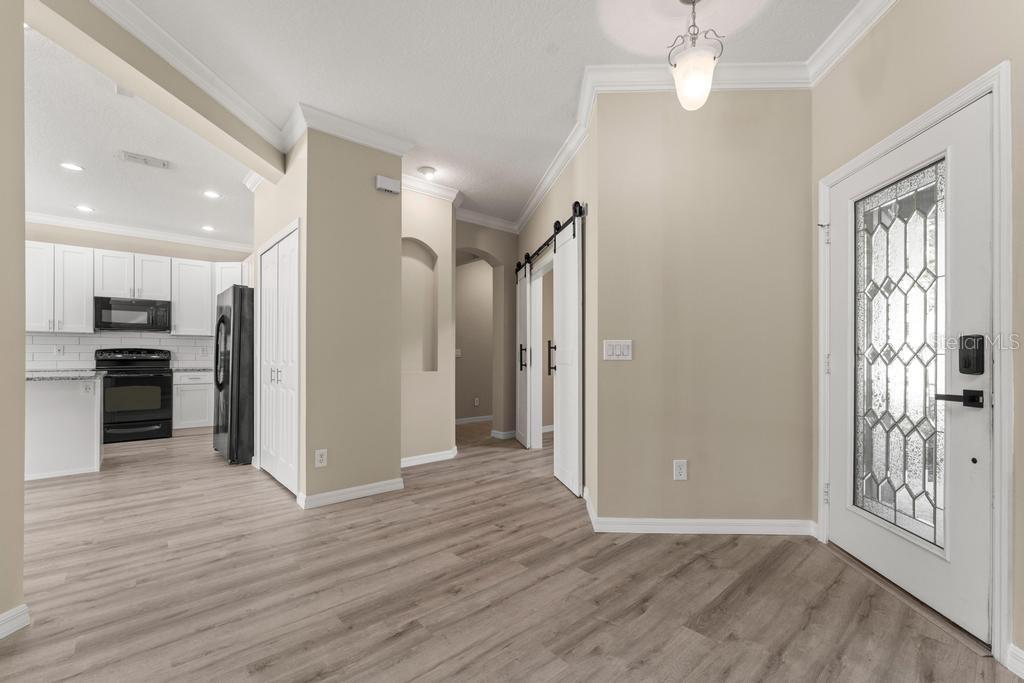 An entryway with light wood-look flooring, a white front door, and a view of the kitchen — 868 STONECHASE LANE, LAKE MARY, FL