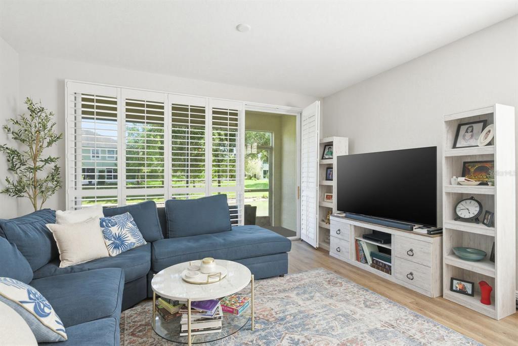 A living room features a blue sectional sofa, a television, and white plantation shutters — 336 HARBOR RIDGE DRIVE, PALM HARBOR, FL