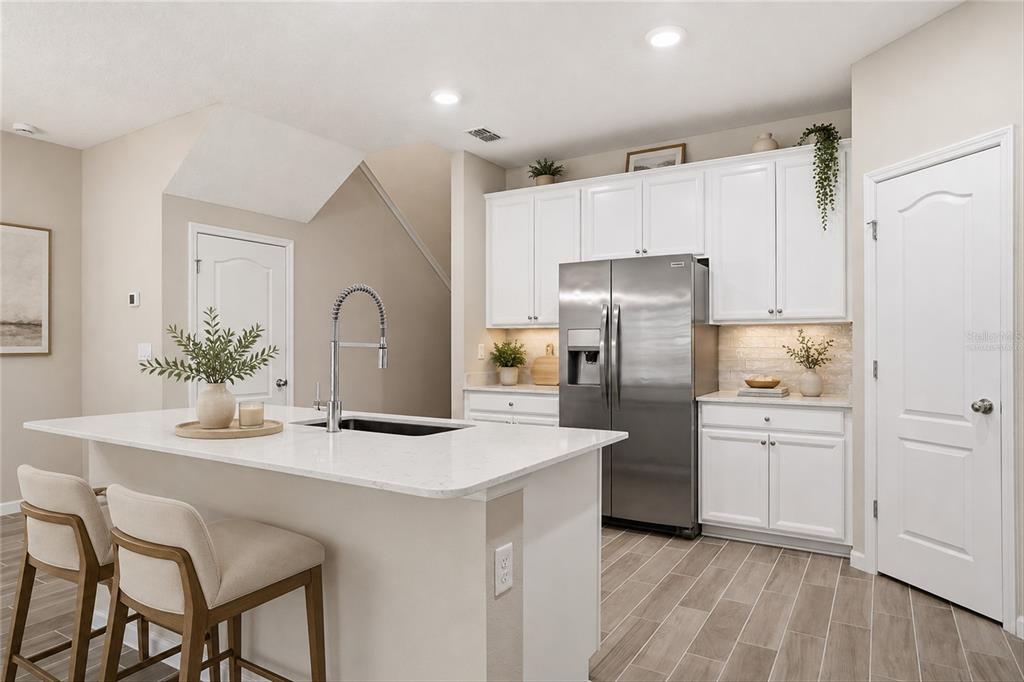 A kitchen features white cabinets, stainless steel appliances, a quartz island, and wood-look tile flooring — 1680 POTTSBURG POINT DRIVE, JACKSONVILLE, FL