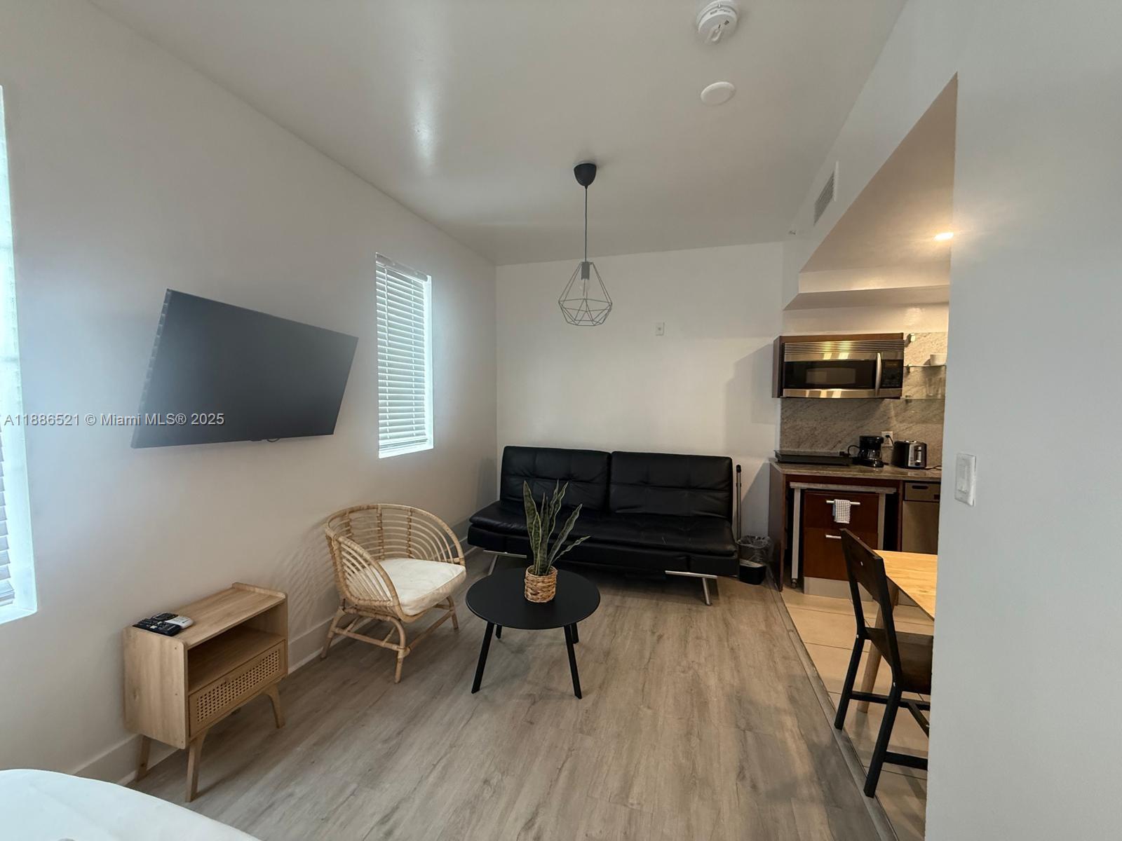A small living area features a black sofa, a rattan chair, and an adjacent kitchenette — 1036 Ocean Dr # B309, Miami Beach FL 33139, MIAMI BEACH, FL