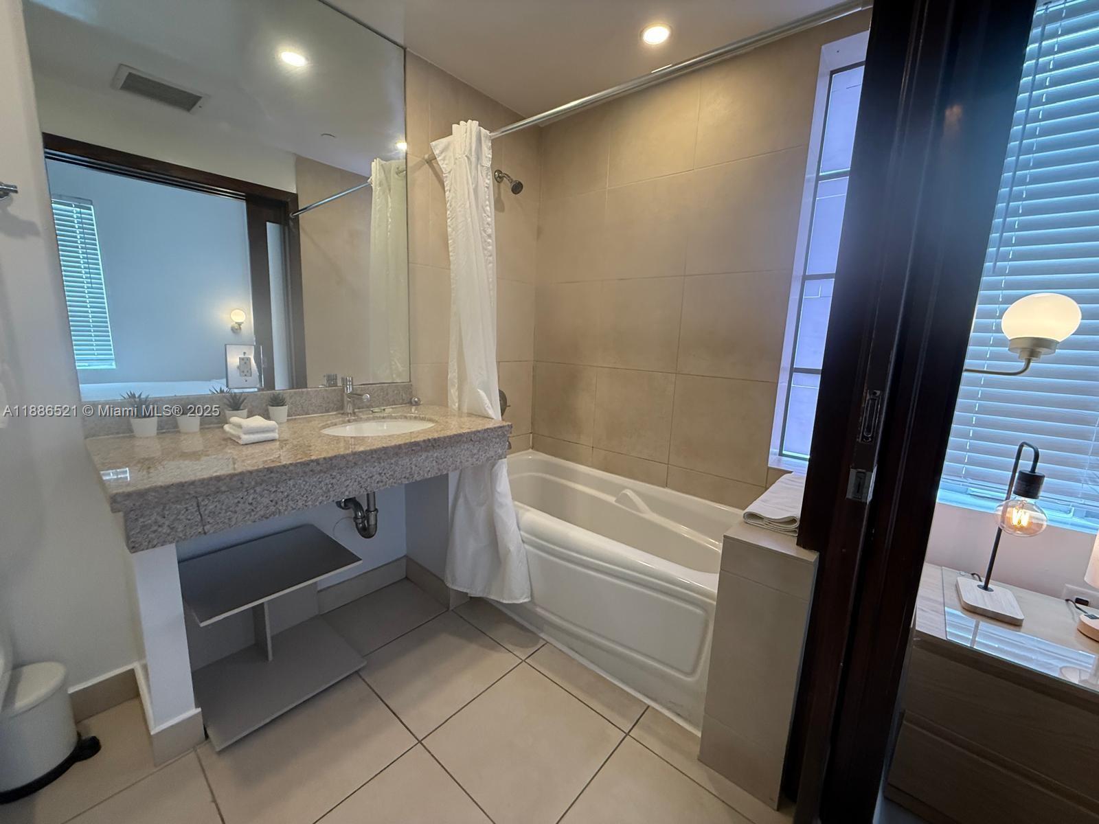 A bathroom features a granite vanity, a bathtub with a shower, and beige tile flooring — 1036 Ocean Dr # B309, Miami Beach FL 33139, MIAMI BEACH, FL