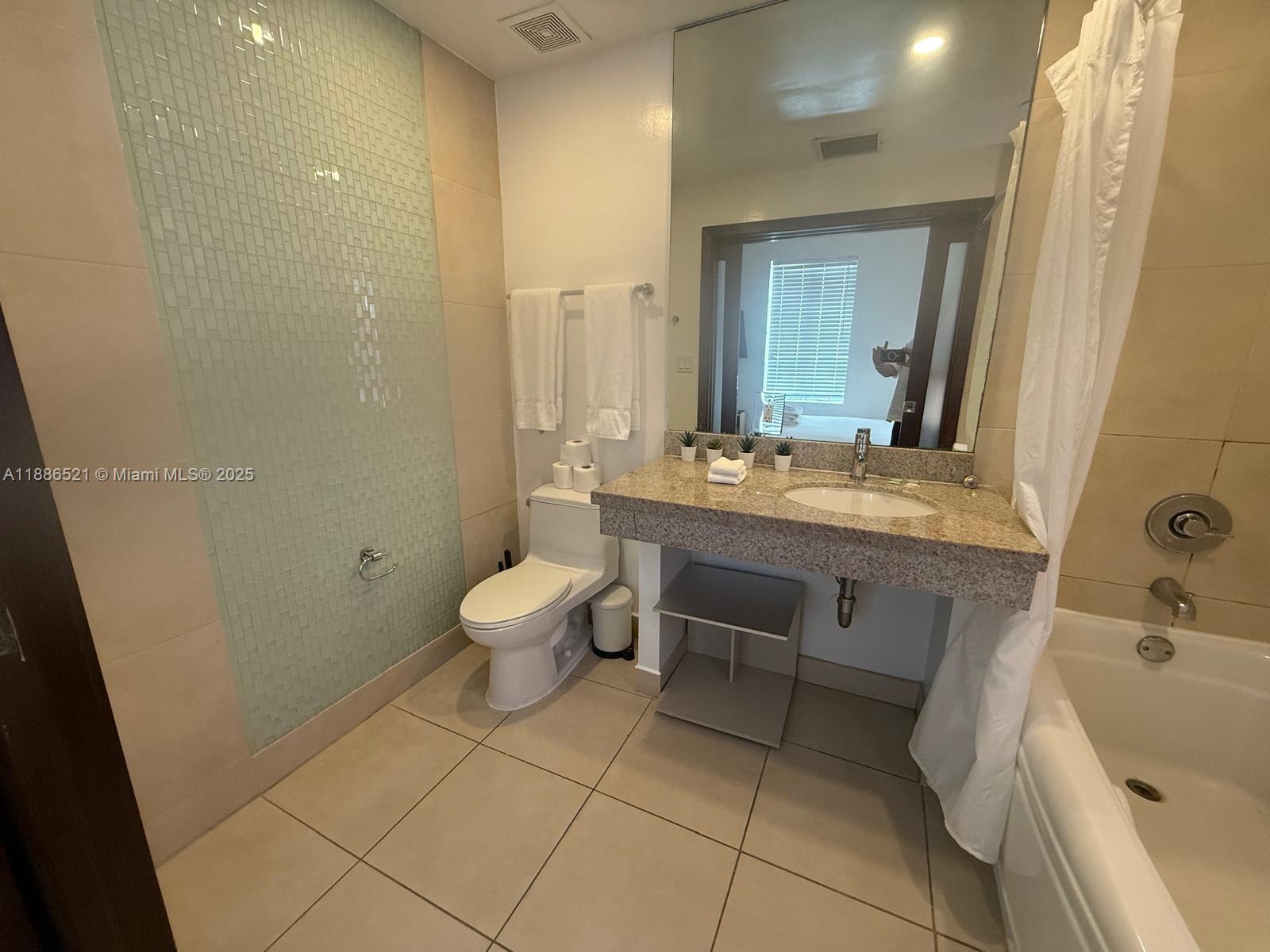 A bathroom features a granite vanity, a toilet, a bathtub, and a glass-tiled accent wall — 1036 Ocean Dr # B309, Miami Beach FL 33139, MIAMI BEACH, FL