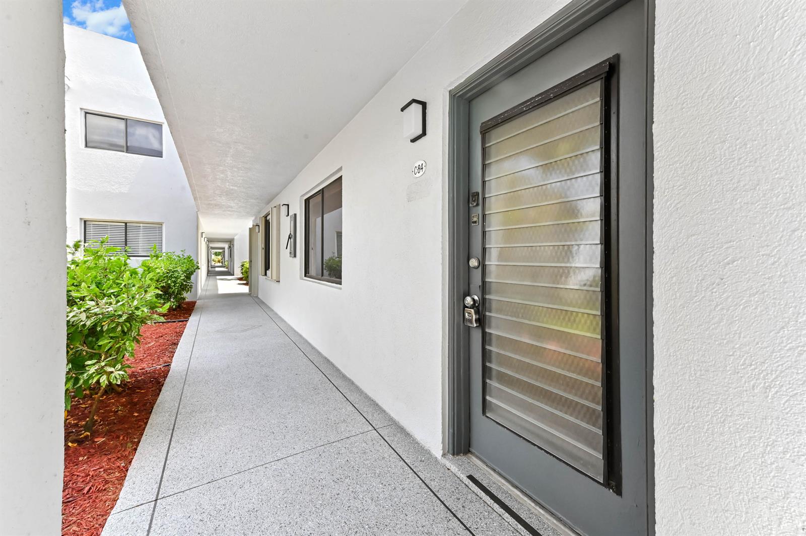 An outdoor walkway leads past a gray door with a louvered glass window insert — 15054 Ashland Way # 84, Delray Beach FL 33484, DELRAY BEACH, FL