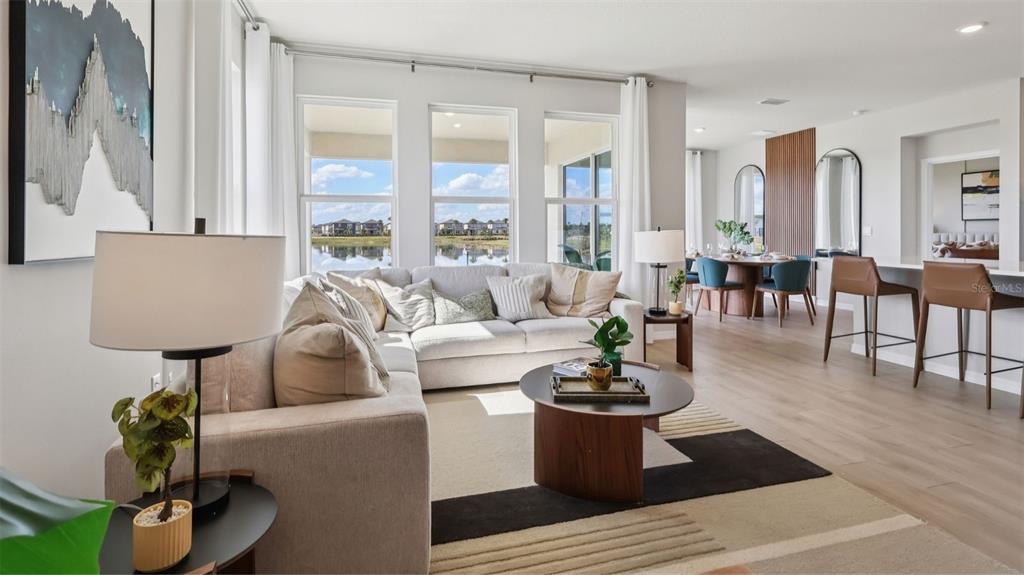 A bright living room features a sectional sofa, a coffee table, and large windows overlooking water — 3046 KINGSMAN TRAIL, ORMOND BEACH, FL