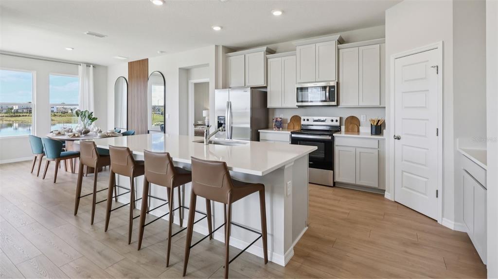 A modern kitchen features a large quartz island, light gray cabinetry, and stainless steel appliances — 3046 KINGSMAN TRAIL, ORMOND BEACH, FL