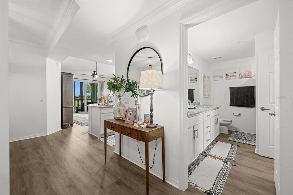 A hallway leads to a kitchen and bathroom with wood-look flooring and white cabinetry — 43030 GREENWAY BOULEVARD UNIT 428, PUNTA GORDA, FL