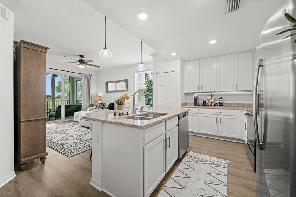 A kitchen with white cabinets and granite countertops overlooks a living area with patio access — 43030 GREENWAY BOULEVARD UNIT 428, PUNTA GORDA, FL