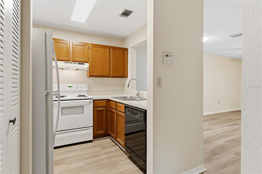 A kitchen features wood cabinets, white appliances, a black dishwasher, and light-colored wood flooring — 4526 SW 44TH LANE UNIT 4526, GAINESVILLE, FL
