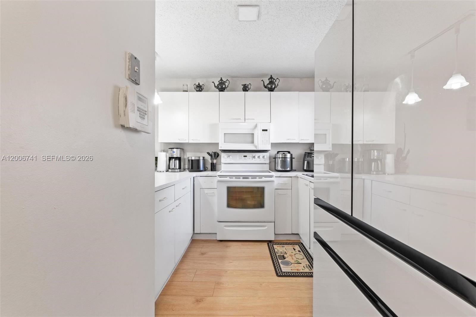 A galley kitchen features white cabinets, white appliances, and light wood-look flooring — 6235 Kendale Lakes Cir # 247, Miami FL 33183, MIAMI, FL